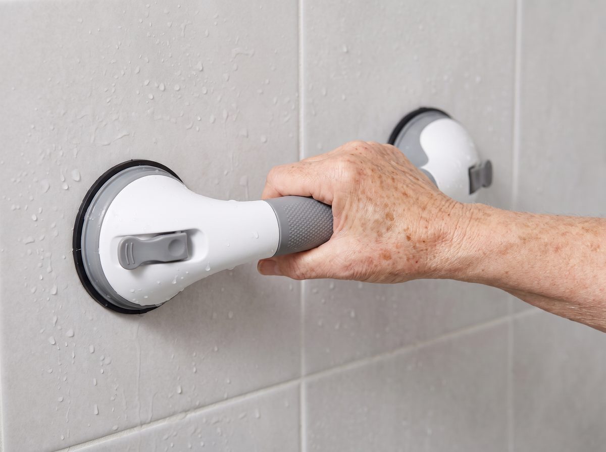 A hand gripping a Mantle Grip safety handle mounted on wet shower tile