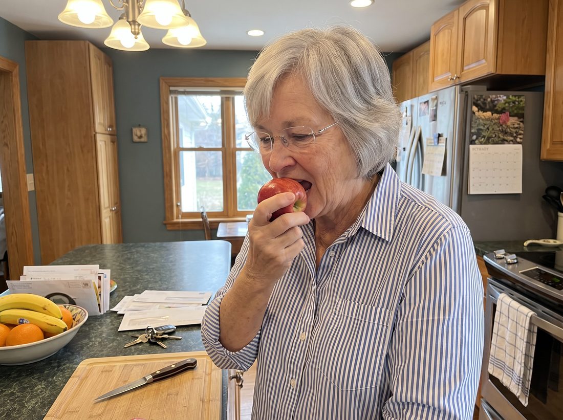 Carol biting into a whole apple in her kitchen